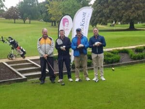 1. Group of four men standing on a golf course with golf bags and clubs, smiling and enjoying a game.