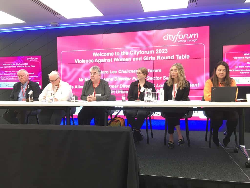 Prominent panel of speakers discussing violence against women and girls at Cityforum 2023 round table event in a modern conference room.