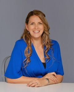 Smiling woman in blue professional outfit sitting at desk, businesswoman portrait, confident female professional, corporate headshot for career and success, friendly female executive image.
