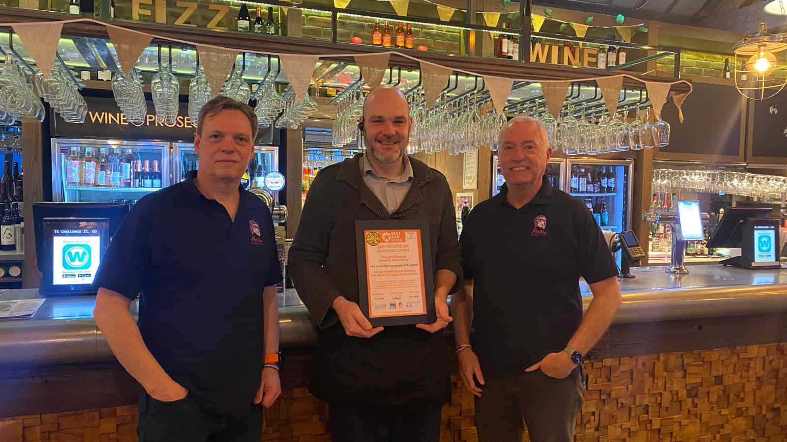 Certified pub team celebrating award recognition at the bar, showcasing expertise in hospitality, customer service, and quality beverage offerings, with a warm and welcoming atmosphere.