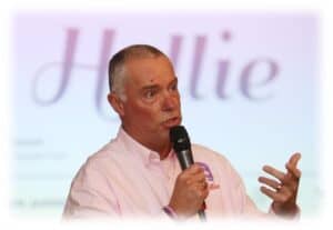 Dynamic speaker holding a microphone during a presentation, promoting personal development and motivation at Hollie Gazzard Foundation event.